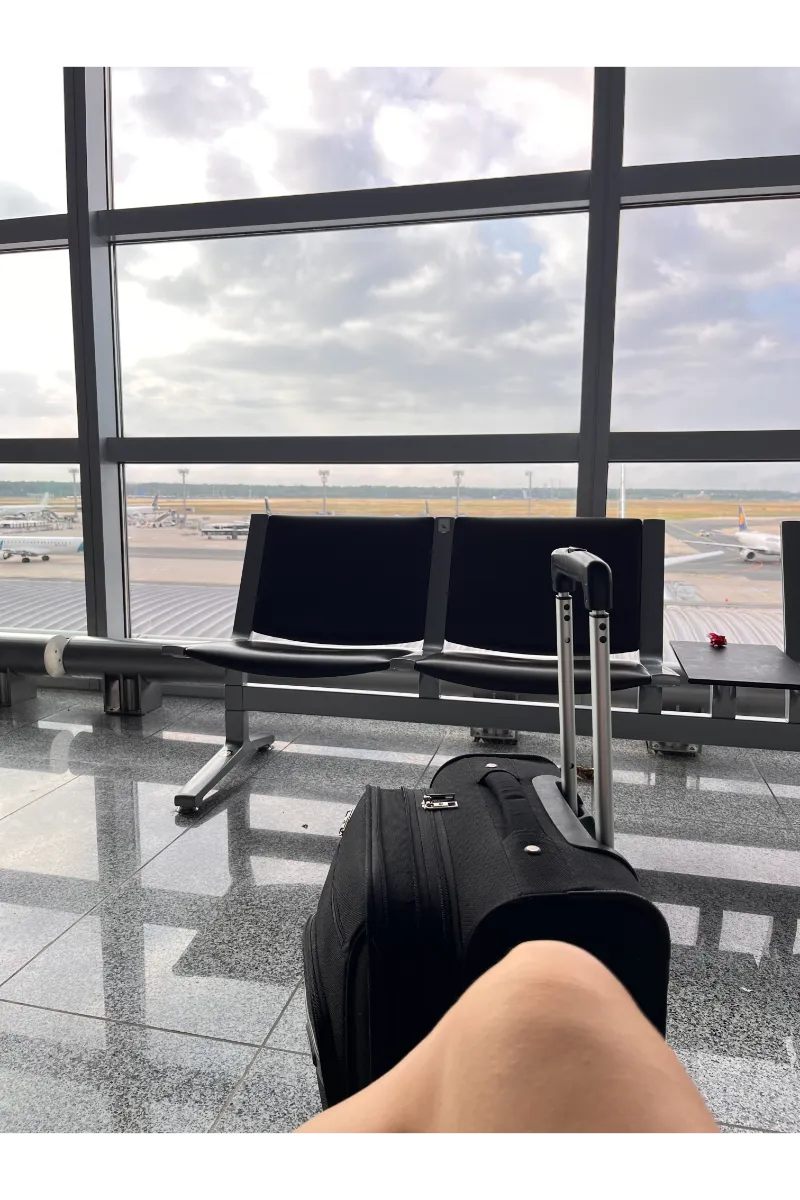 A person sitting at the airport with a small suitcase in front.