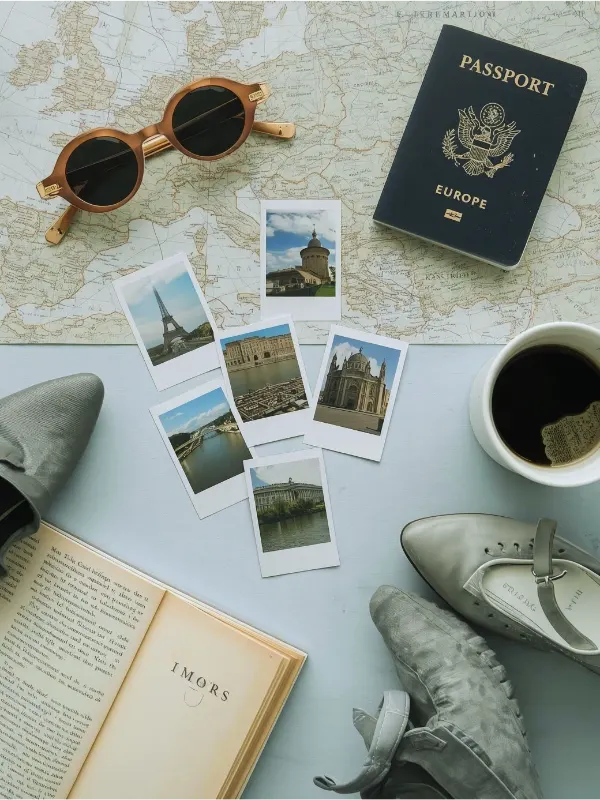 Vertical photo (800x1200) showing a moodboard-style flat lay with Europe travel inspiration_ map, passport, sunglasses, polaroid photos, cute shoes, travel guidebook, and a coffee cup. Light blue tones, modern, fe