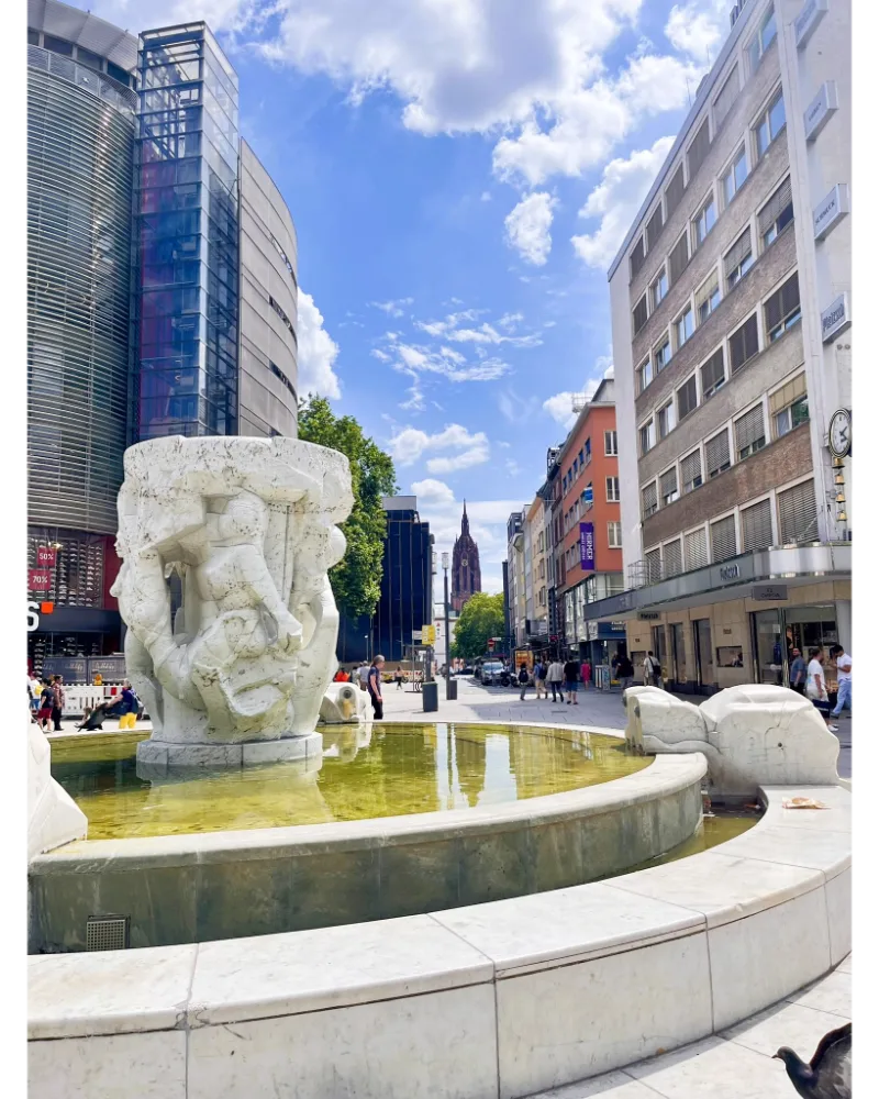 Sculpture and fountain in Zeil with Frankfurt Cathedral (Kaiserdom) visible in the background.